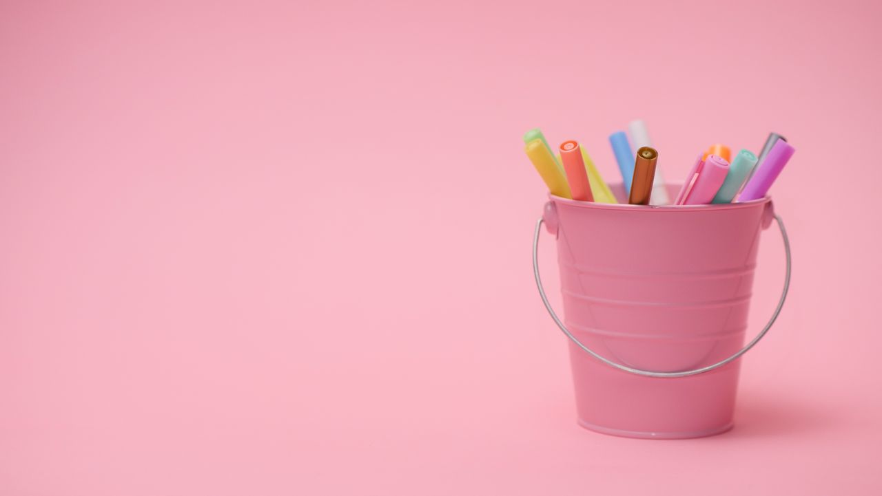 about-07 Vibrant colored markers in a small pink bucket on a pastel pink background with copyspace.