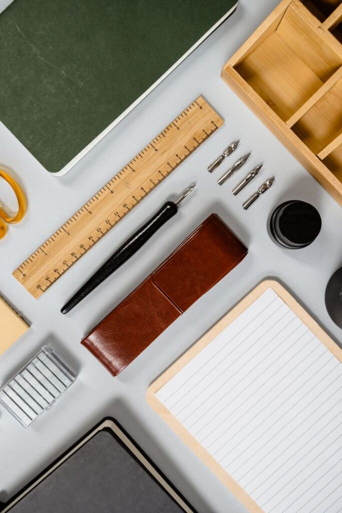 Top view of stationery essentials including notebooks, ruler, and ink on a white background.